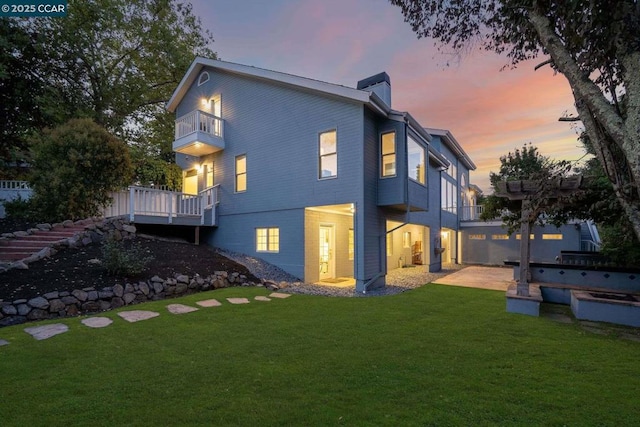 back house at dusk with a balcony, a yard, and a patio