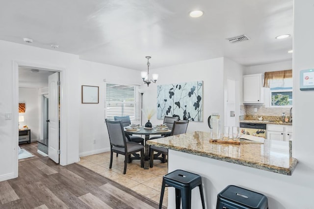 kitchen featuring light stone countertops, dishwashing machine, decorative light fixtures, white cabinetry, and plenty of natural light