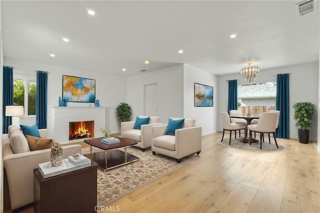 living room with a notable chandelier, a brick fireplace, and light hardwood / wood-style floors