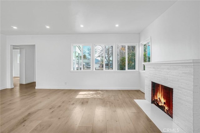 unfurnished living room featuring plenty of natural light, a brick fireplace, and light hardwood / wood-style floors