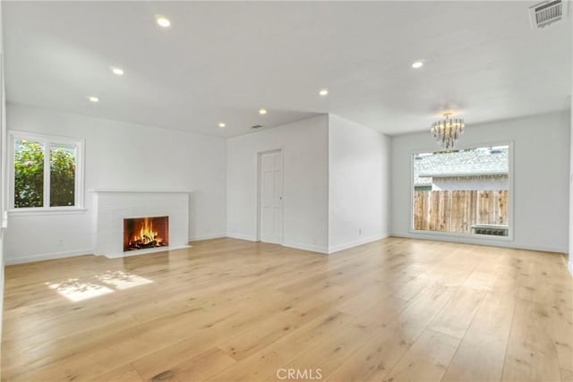 unfurnished living room with light wood-type flooring, a chandelier, and a brick fireplace