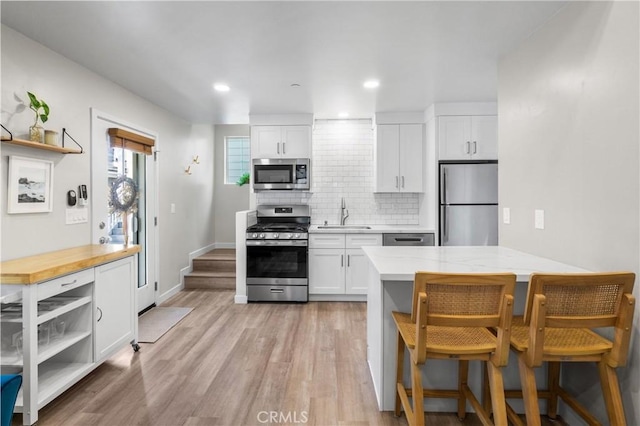 kitchen featuring appliances with stainless steel finishes, a sink, white cabinetry, open shelves, and backsplash