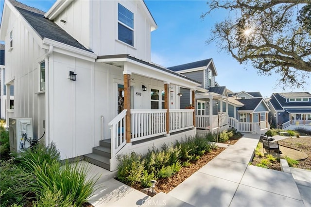 view of front of home featuring covered porch, a residential view, board and batten siding, and ac unit