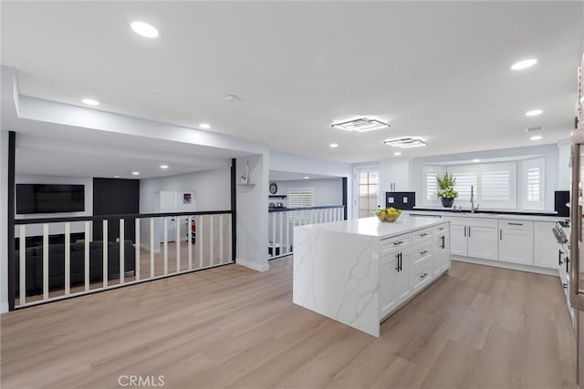 kitchen with white cabinetry, sink, a center island, light stone countertops, and light wood-type flooring