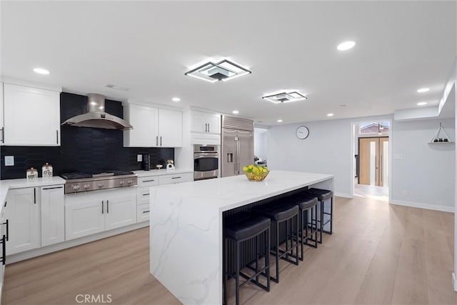 kitchen with white cabinetry, a center island, and wall chimney exhaust hood