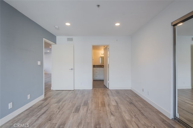 unfurnished bedroom with ensuite bathroom and light hardwood / wood-style flooring