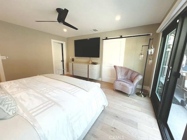 bedroom with ceiling fan, a barn door, and light hardwood / wood-style flooring