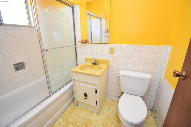 full bathroom featuring vanity, toilet, bath / shower combo with glass door, and tile walls