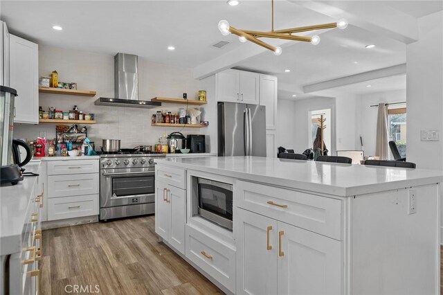 kitchen featuring appliances with stainless steel finishes, wall chimney exhaust hood, white cabinetry, decorative backsplash, and light wood-type flooring