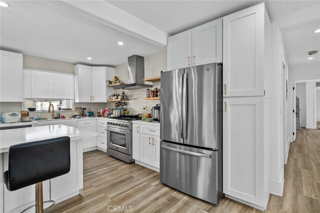 kitchen featuring white cabinetry, wall chimney range hood, stainless steel appliances, decorative backsplash, and light wood-type flooring