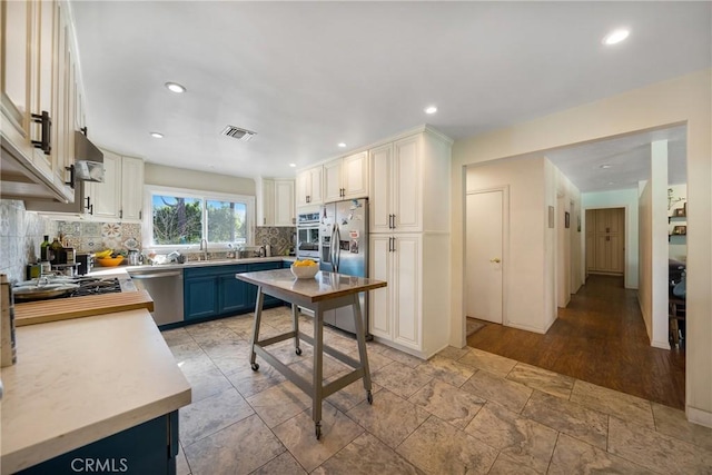 kitchen with blue cabinets, white cabinetry, appliances with stainless steel finishes, and decorative backsplash