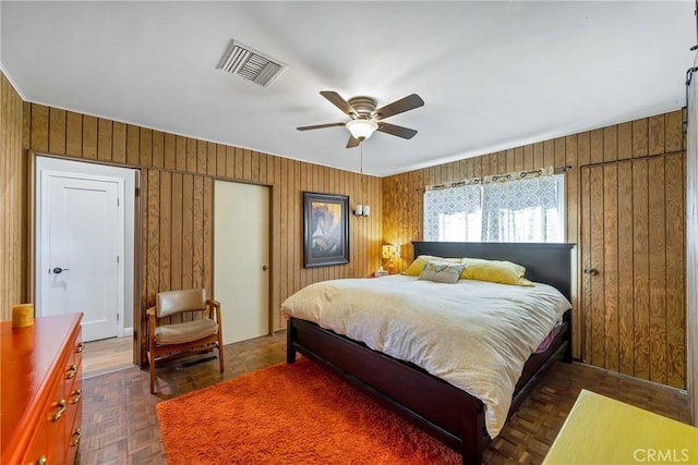 bedroom featuring ceiling fan, dark parquet flooring, and wooden walls