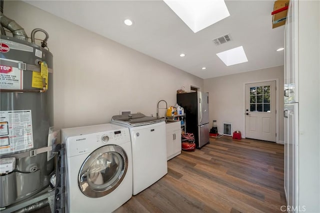 clothes washing area with a skylight, washing machine and clothes dryer, dark hardwood / wood-style flooring, gas water heater, and cabinets