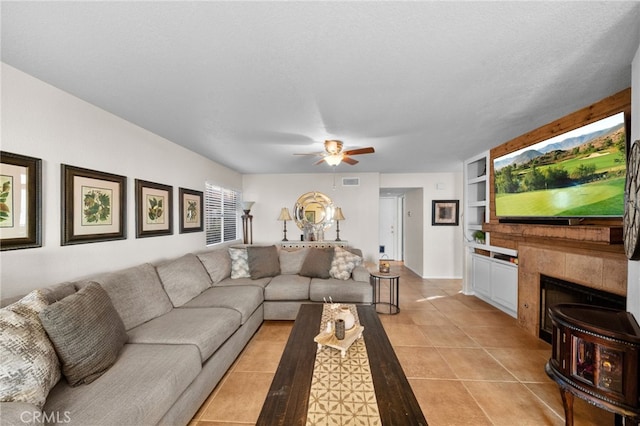 tiled living room featuring built in features, a textured ceiling, a tiled fireplace, and ceiling fan