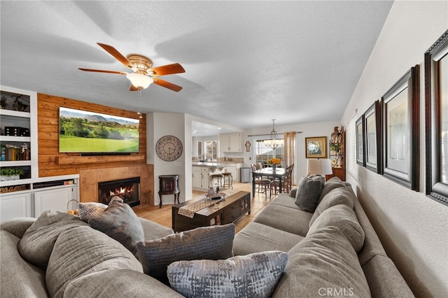 living room featuring ceiling fan with notable chandelier, built in features, a textured ceiling, and light tile patterned flooring