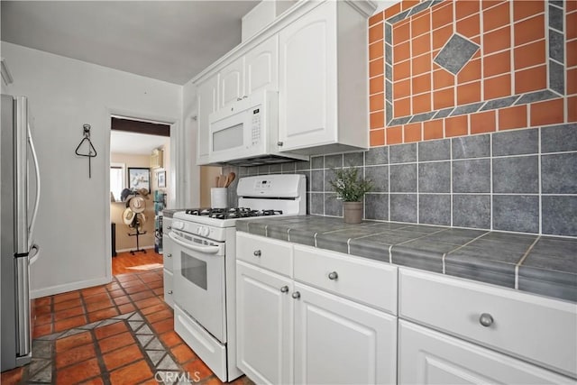 kitchen with white appliances, white cabinetry, backsplash, tile counters, and dark tile patterned flooring