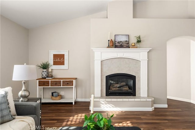 living room with dark hardwood / wood-style flooring, a tiled fireplace, and vaulted ceiling