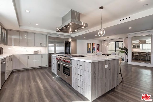 kitchen featuring decorative light fixtures, premium appliances, dark hardwood / wood-style flooring, a raised ceiling, and island exhaust hood