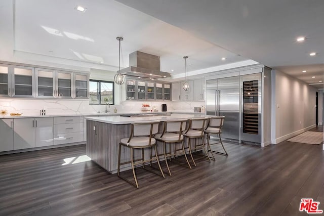 kitchen with island range hood, stainless steel built in refrigerator, hanging light fixtures, a large island, and dark wood-type flooring