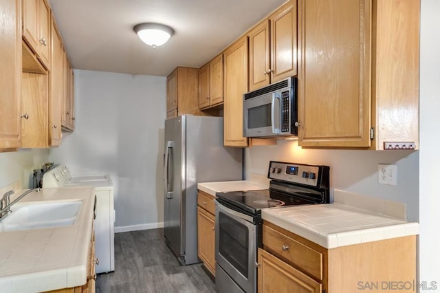 kitchen with appliances with stainless steel finishes, sink, dark wood-type flooring, washing machine and dryer, and tile countertops