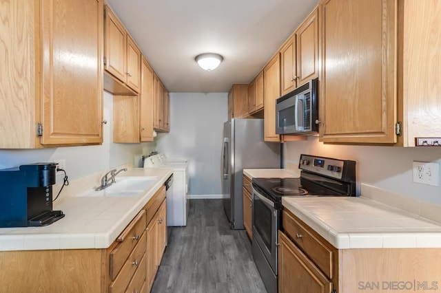 kitchen featuring sink, tile counters, appliances with stainless steel finishes, and dark hardwood / wood-style flooring