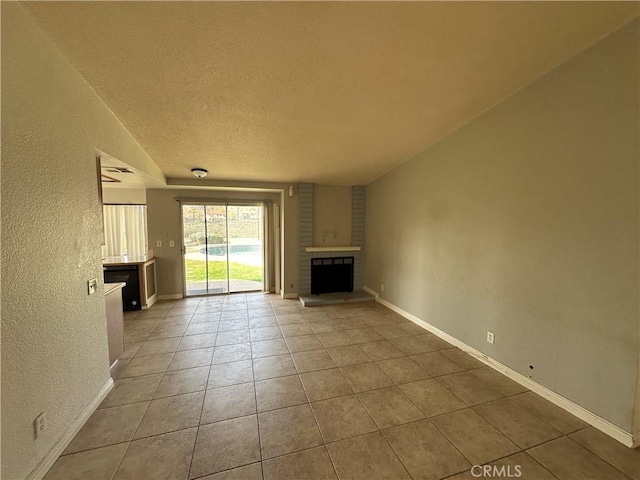 unfurnished living room with baseboards, a fireplace, a textured wall, tile patterned floors, and a textured ceiling