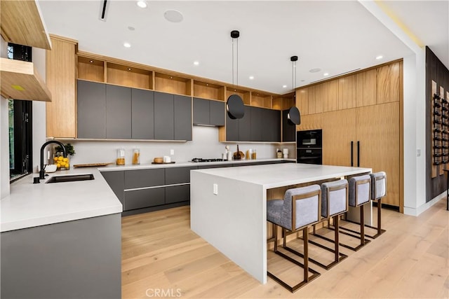 kitchen featuring a kitchen island, decorative light fixtures, light hardwood / wood-style floors, sink, and gray cabinetry