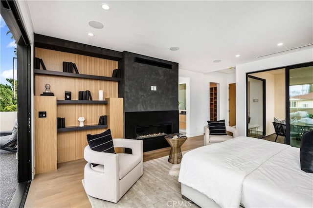 bedroom with access to outside, light hardwood / wood-style flooring, ensuite bathroom, and a large fireplace