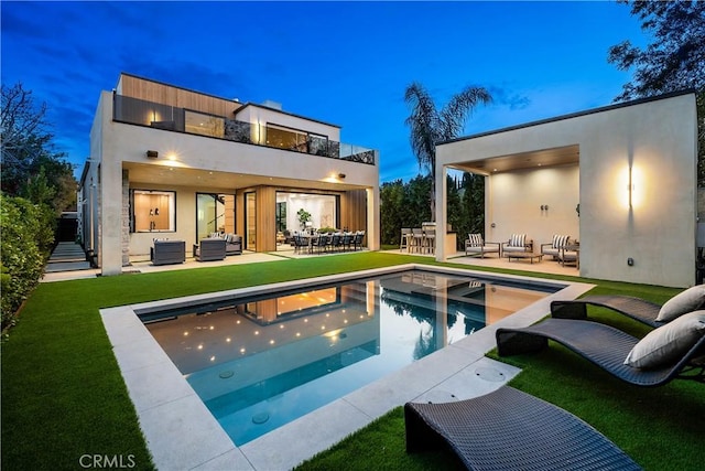 back house at dusk with an outdoor living space, a patio area, a yard, and a balcony