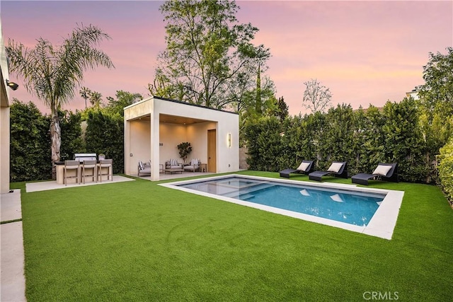 pool at dusk with a patio area, exterior bar, and a yard