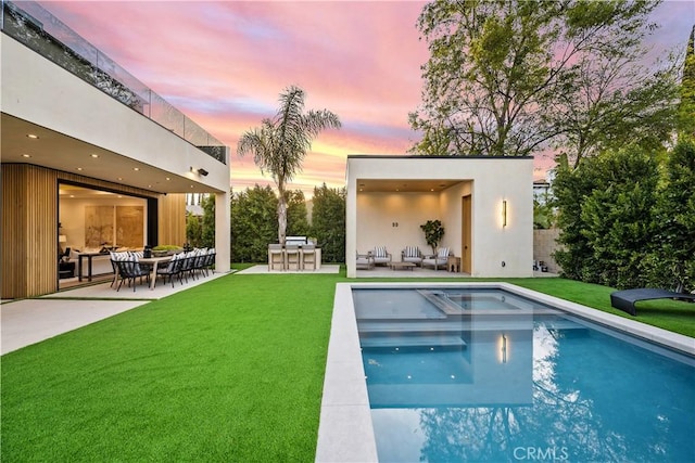 pool at dusk featuring a bar, a lawn, an outdoor living space, and a patio