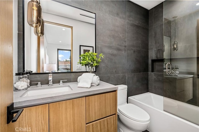 full bathroom with combined bath / shower with glass door, toilet, vanity, and tile walls