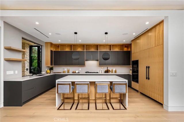 kitchen featuring pendant lighting, light hardwood / wood-style flooring, a large island, oven, and a breakfast bar area