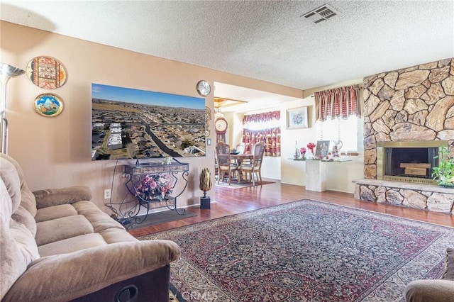 living room featuring a stone fireplace, hardwood / wood-style floors, and a textured ceiling