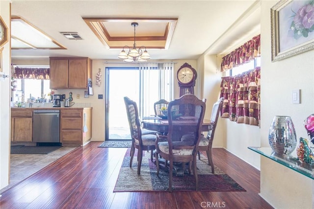 dining room featuring a healthy amount of sunlight, a tray ceiling, dark hardwood / wood-style flooring, and a notable chandelier