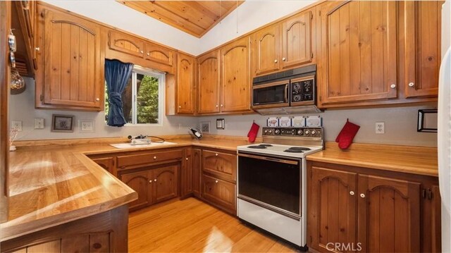 kitchen with butcher block counters, white electric range, sink, light hardwood / wood-style flooring, and vaulted ceiling