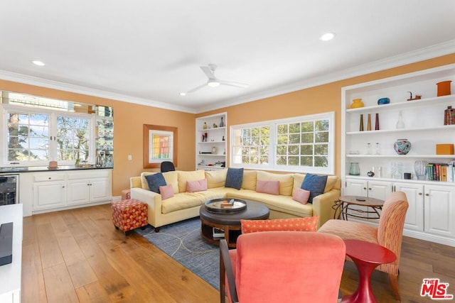 living room featuring crown molding, light hardwood / wood-style flooring, built in shelves, and ceiling fan