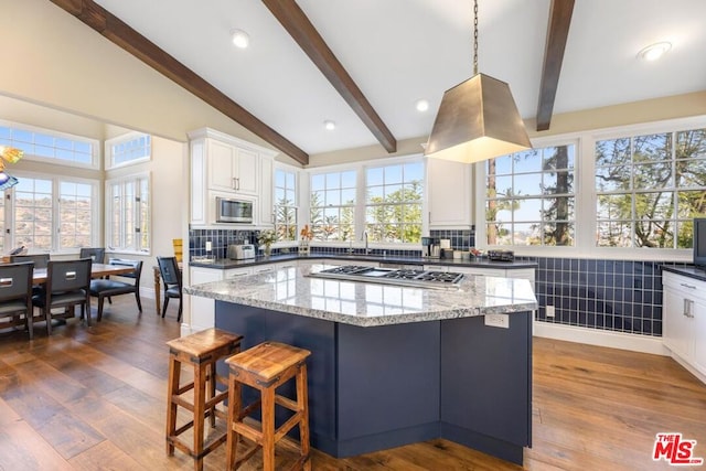 kitchen featuring light stone countertops, hardwood / wood-style floors, a center island, white cabinetry, and stainless steel appliances