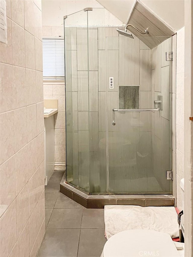 bathroom with tile walls, toilet, a shower with door, and tile patterned flooring