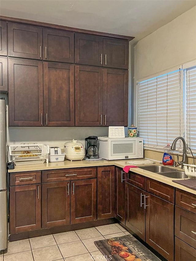 kitchen featuring sink, dark brown cabinetry, light tile patterned floors, and refrigerator