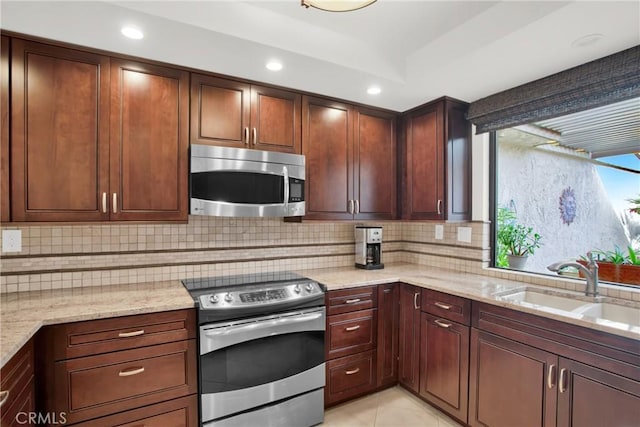 kitchen featuring sink, backsplash, light tile patterned floors, stainless steel appliances, and light stone countertops