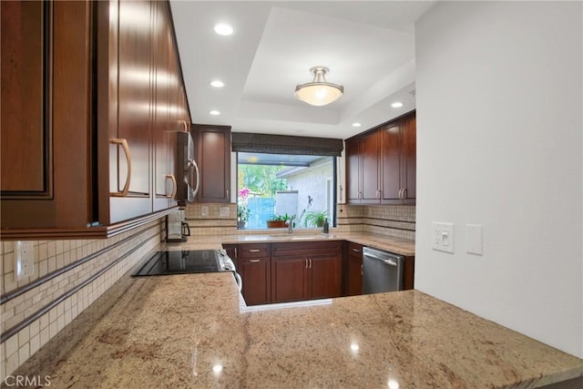 kitchen with appliances with stainless steel finishes, kitchen peninsula, sink, a tray ceiling, and light stone countertops