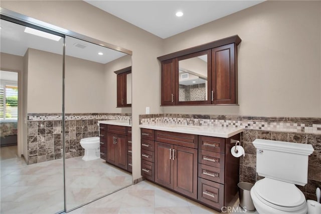 bathroom with tile walls, vanity, and toilet