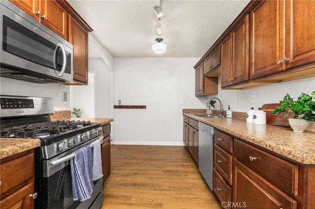 kitchen featuring sink, light stone counters, track lighting, stainless steel appliances, and light hardwood / wood-style floors