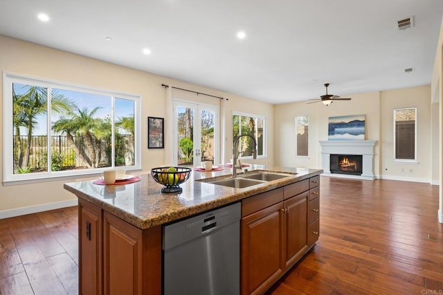 kitchen featuring sink, a kitchen island with sink, stainless steel dishwasher, light stone counters, and dark wood-type flooring