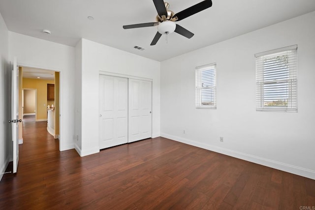 unfurnished bedroom featuring multiple windows, ceiling fan, dark hardwood / wood-style flooring, and a closet