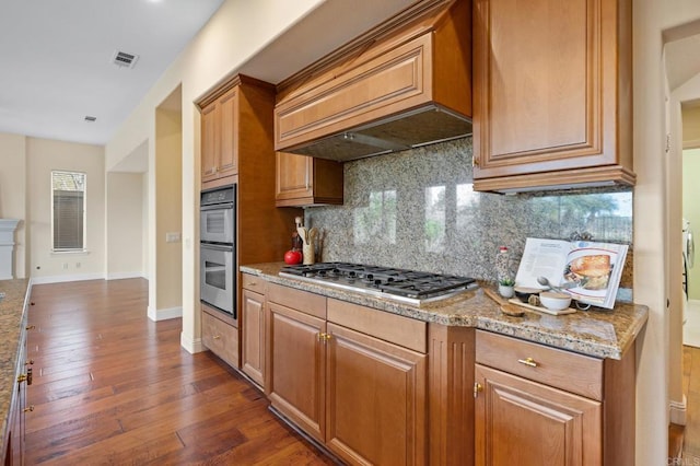 kitchen with custom exhaust hood, tasteful backsplash, dark hardwood / wood-style flooring, stainless steel appliances, and light stone countertops