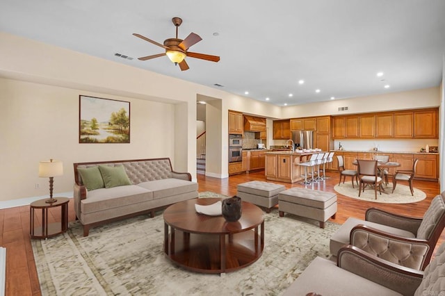 living room featuring sink, ceiling fan, and light wood-type flooring