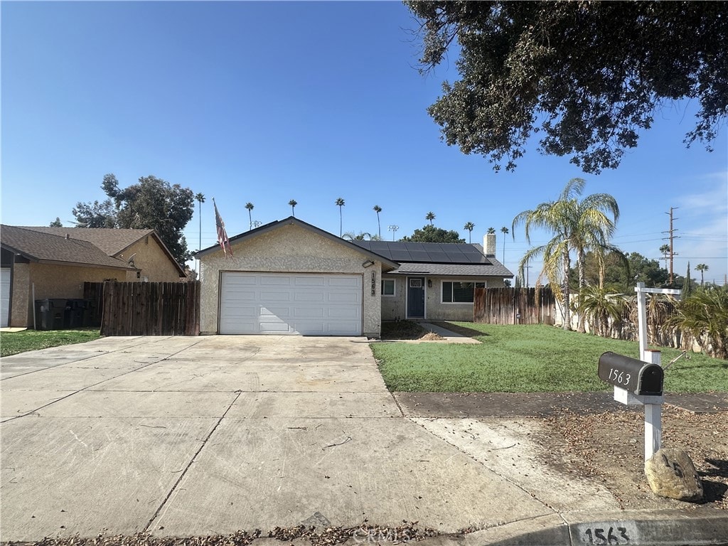 single story home with a garage, a front lawn, and solar panels