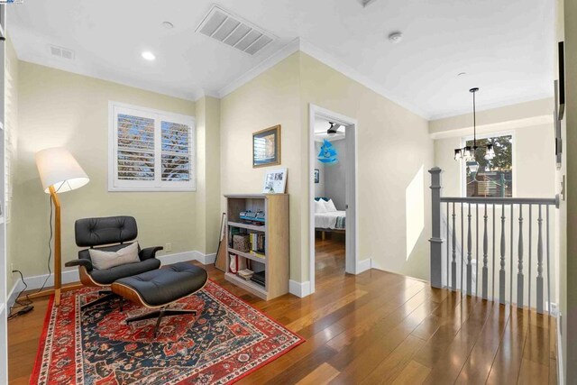 living area with crown molding, hardwood / wood-style floors, and a notable chandelier